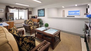 A well-lit living room with a sofa, chairs, a coffee table, and a television displaying 'Travelodge + GO by Wyndham'. - Travelodge by Wyndham Redwood Falls (Redwood Falls)