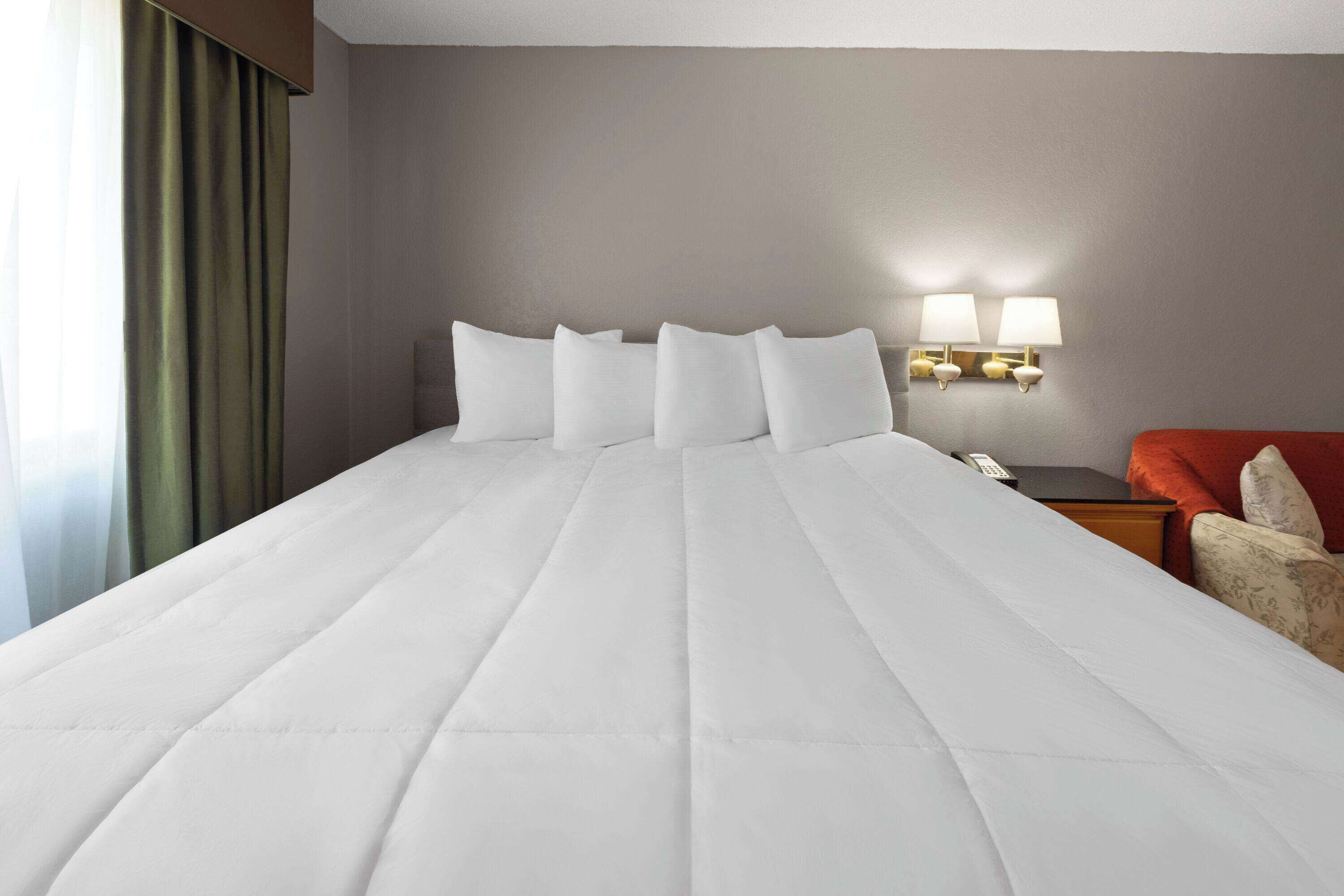 A hotel room with a large bed, a nightstand, a lamp, and a chair.