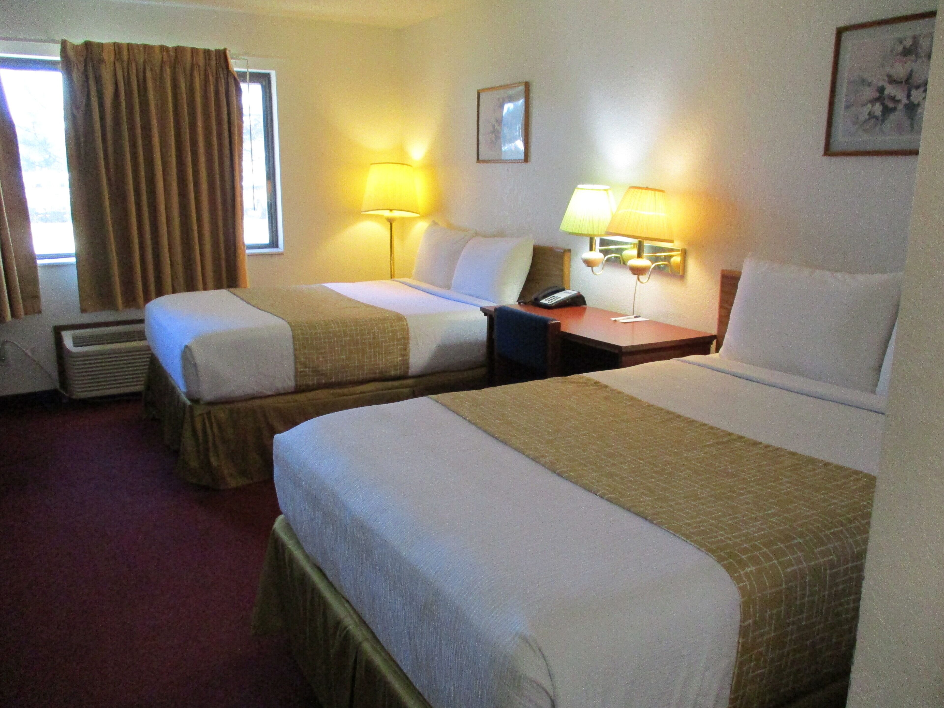 A hotel room with two beds, a desk, a telephone, and two lamps.