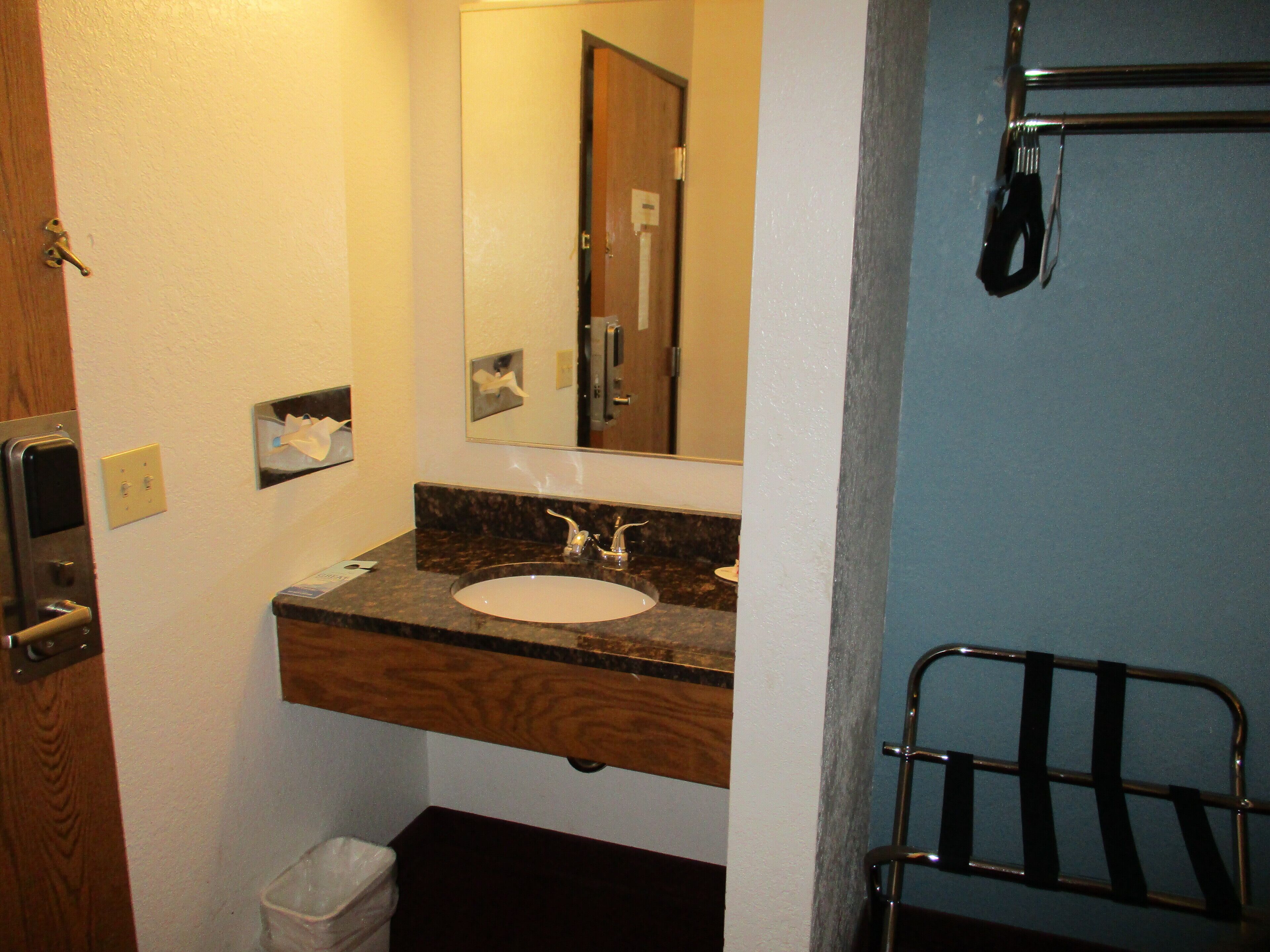A bathroom with a sink, mirror, towel dispenser, and a trash bin.