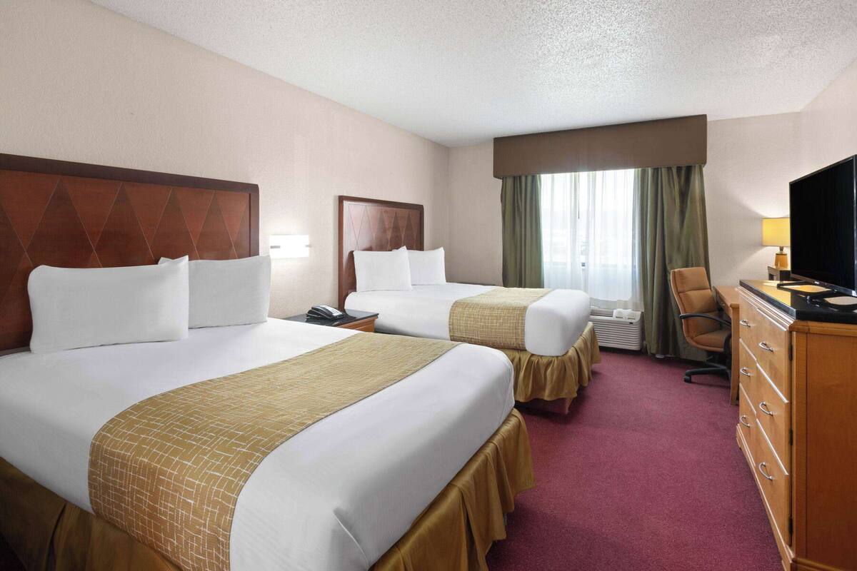 A hotel room with two beds, a desk, a chair, a TV, and a dresser.