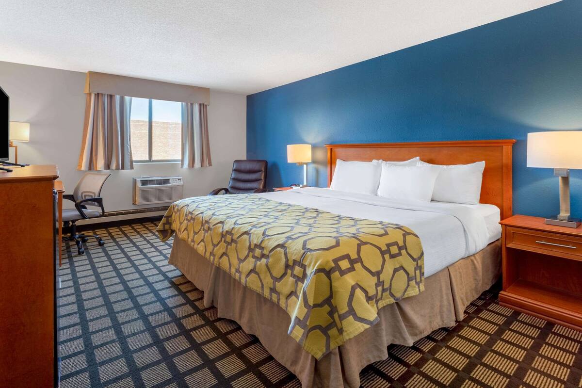 Een hotelkamer met een groot bed, een bureau met stoel, een airconditioning en een raam met gordijnen.