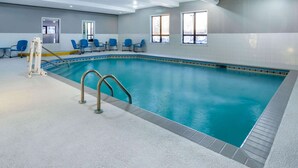 An indoor swimming pool with clear blue water, a ladder, and blue chairs around the pool. - Baymont by Wyndham Rochester Mayo Clinic Area (Rochester)