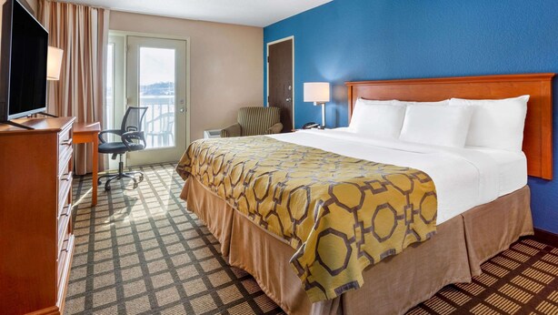 A hotel room with a large bed, a desk with a chair, a television, and a view of the outdoors through a door. - Baymont by Wyndham Rochester Mayo Clinic Area (Rochester)