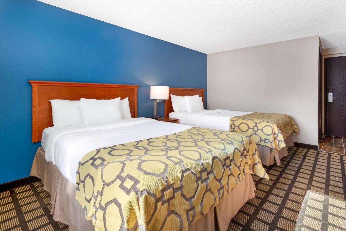 Een hotelkamer met twee bedden, een nachtkastje, een lamp en een kamerbreed tapijt met een patroon.