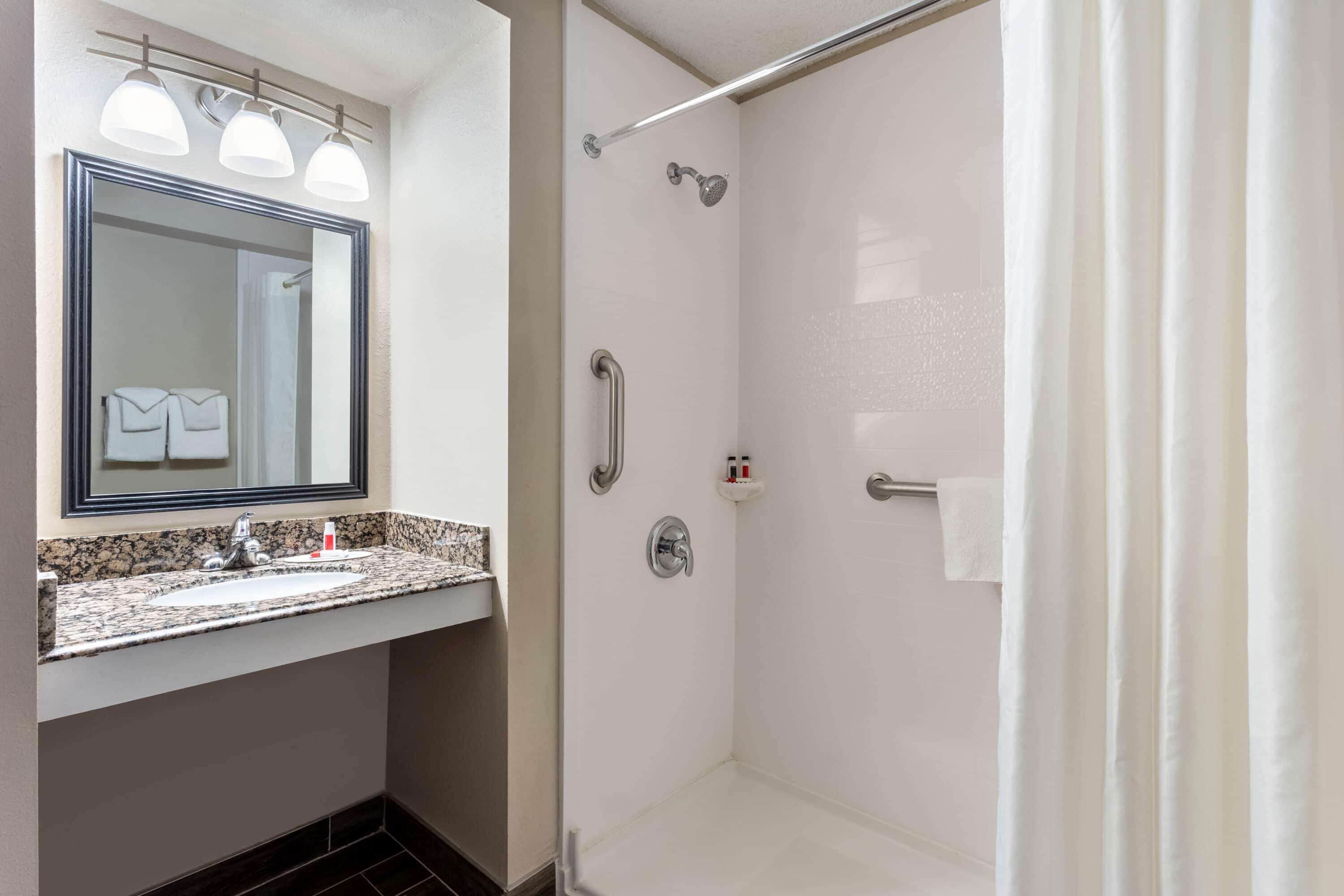 A bathroom with a sink, mirror, and shower.