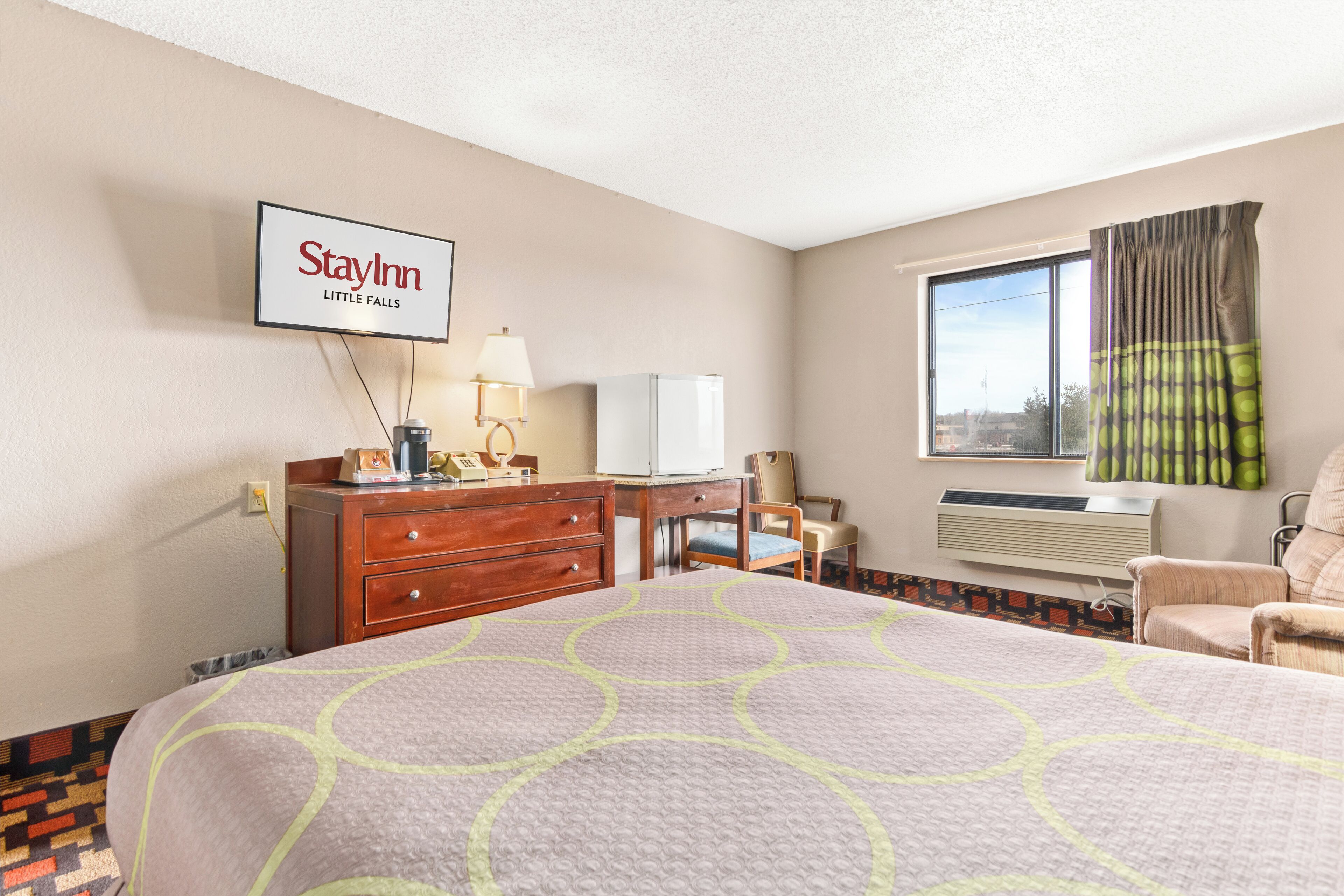 A hotel room with a bed, a desk, a chair, a TV, and a window with curtains.