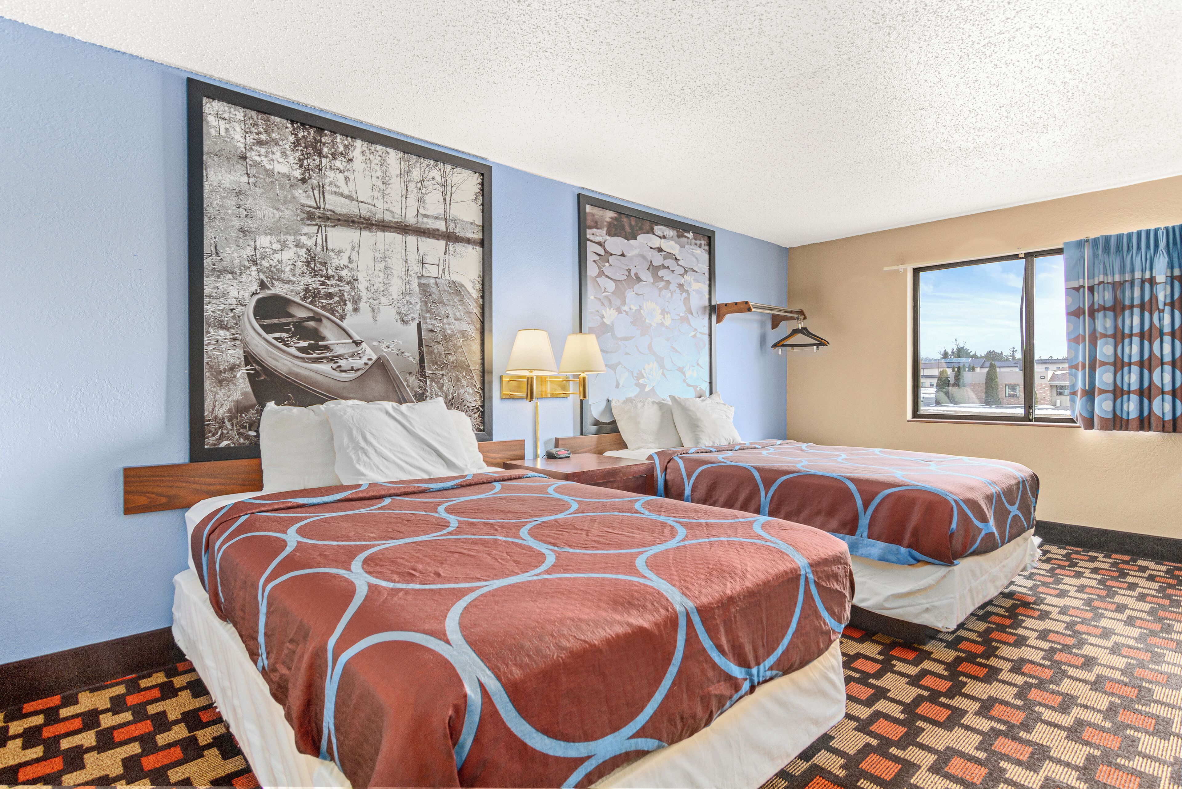 Une chambre d’hôtel avec deux lits, une grande fenêtre avec des rideaux, un sol à motifs et des œuvres d’art accrochées aux murs.