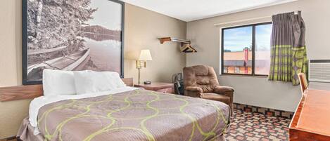 A hotel room with a large bed, a chair, a desk, a window with a view, and a wall-mounted lamp.