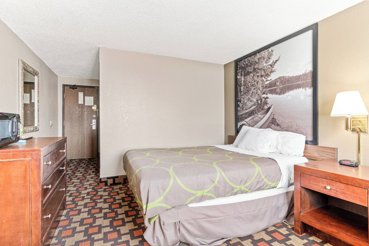 A hotel room with a bed, a dresser, a desk with a lamp, a mirror, and a framed picture on the wall.