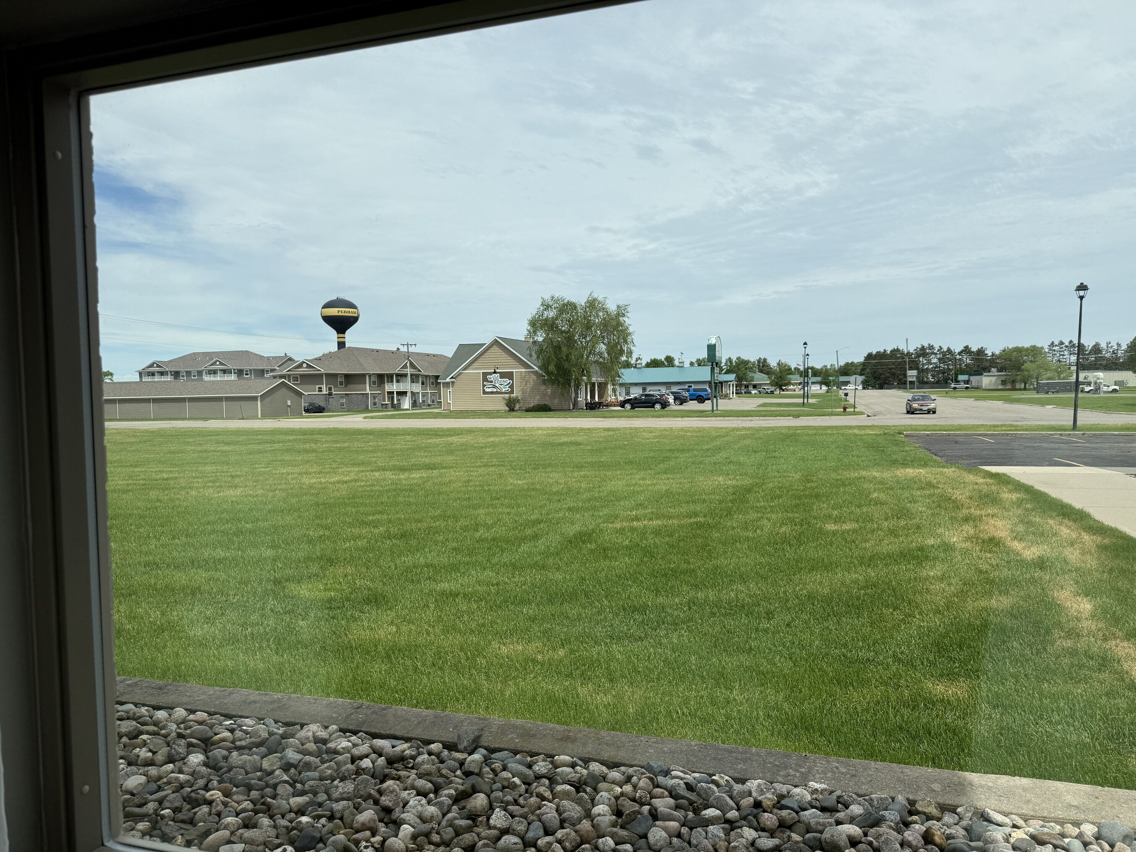 A grassy area with a building in the background, a water tower, and a few cars parked.