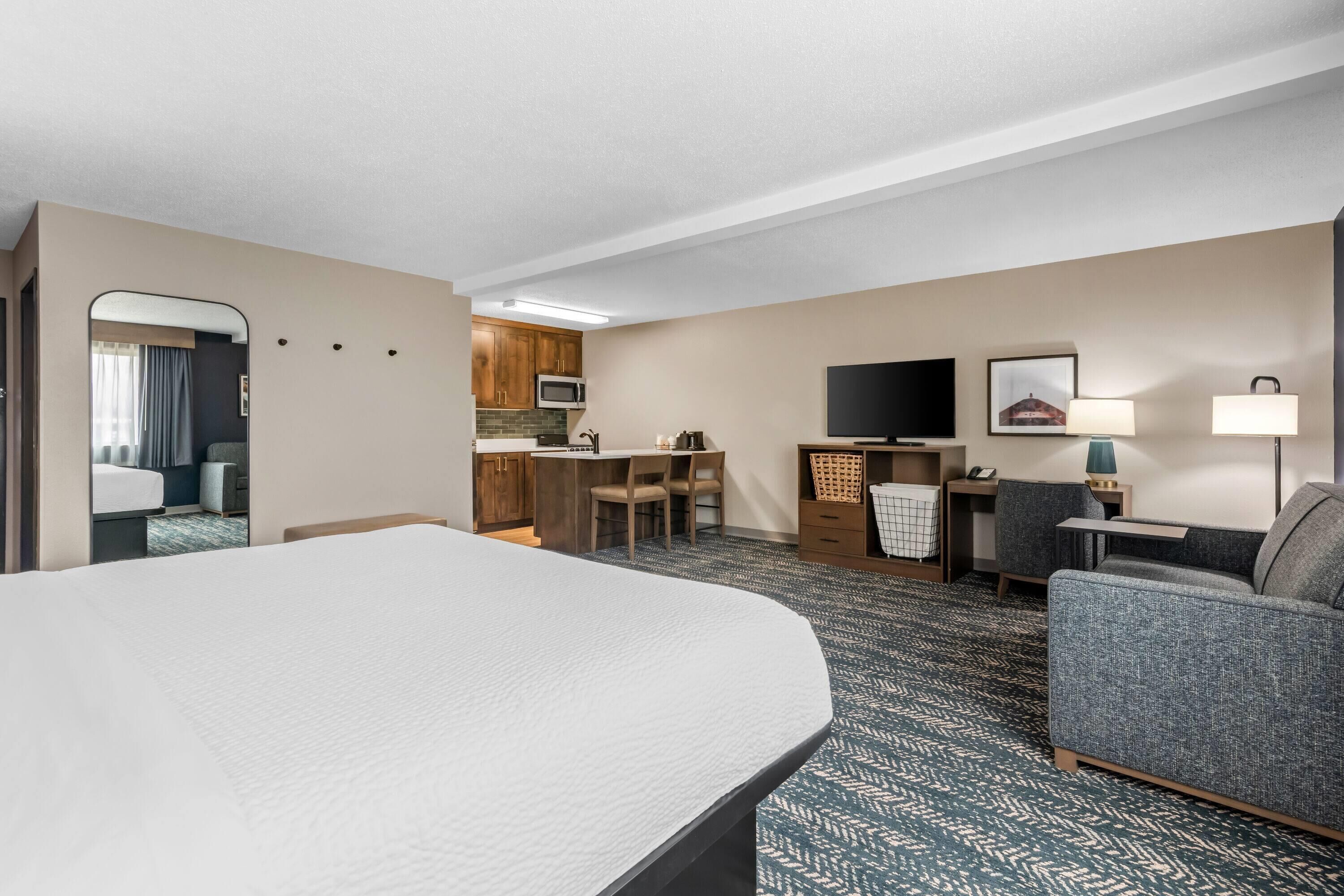 Quarto de hotel com uma cama grande, sofá, escrivaninha com cadeira, televisão e micro-ondas.