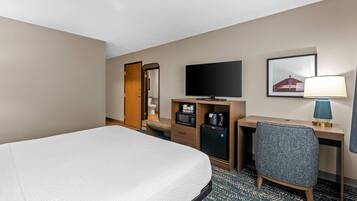 A hotel room with a bed, a desk, a television, a lamp, and a small refrigerator.