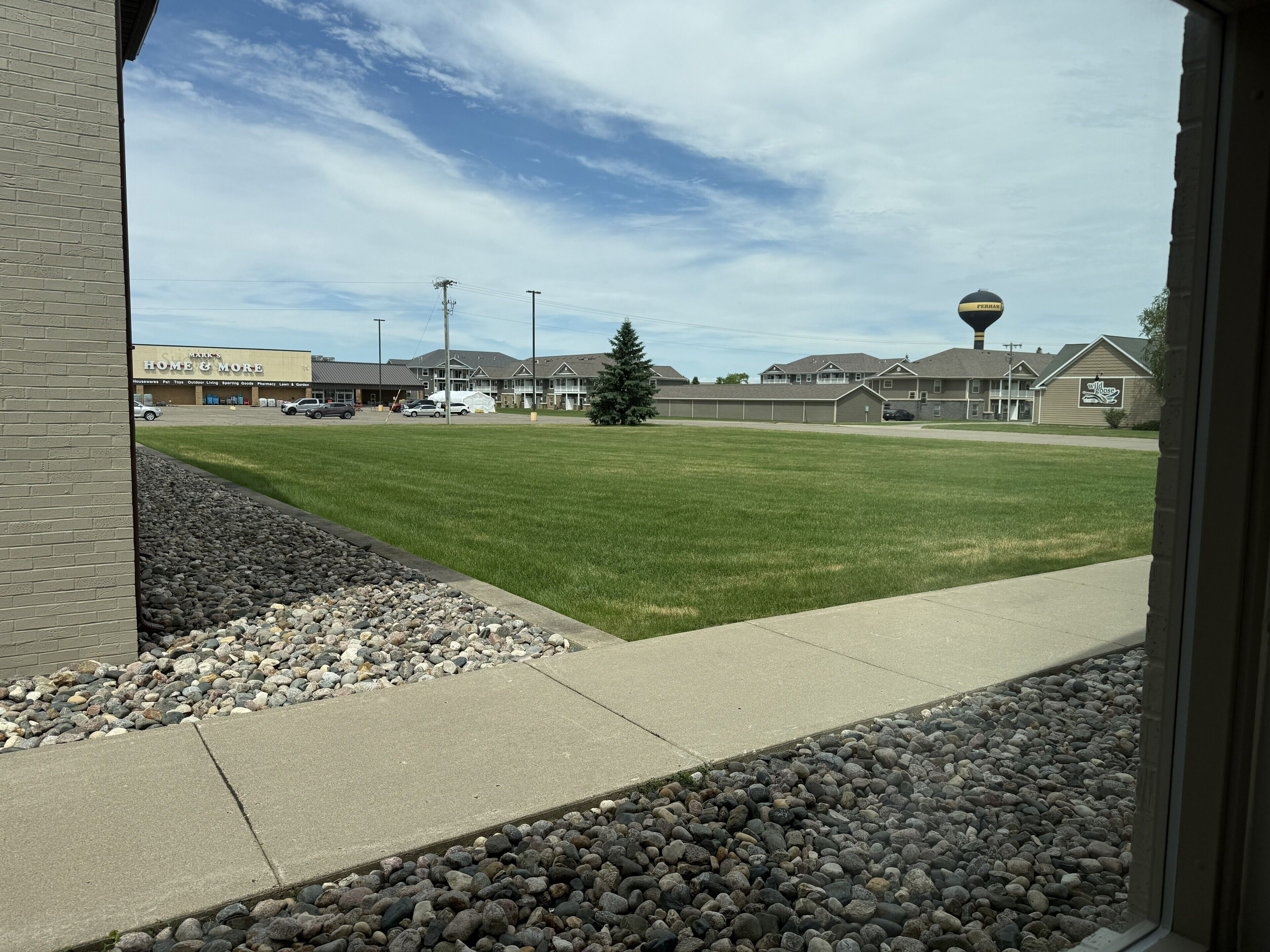 A view of a commercial area with a grassy lawn, a building labeled 'Home & More,' and a water tower in the background.