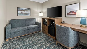 Una habitación de hotel con sofá, escritorio, televisor, lámpara y refrigerador.