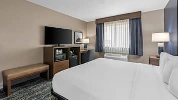 Une chambre d’hôtel avec un grand lit, une télévision, un bureau avec un ordinateur, un banc et une fenêtre avec des rideaux.