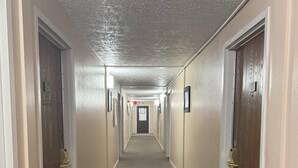 Un couloir avec des portes de chaque côté, un sol recouvert de moquette et un plafond à motifs.