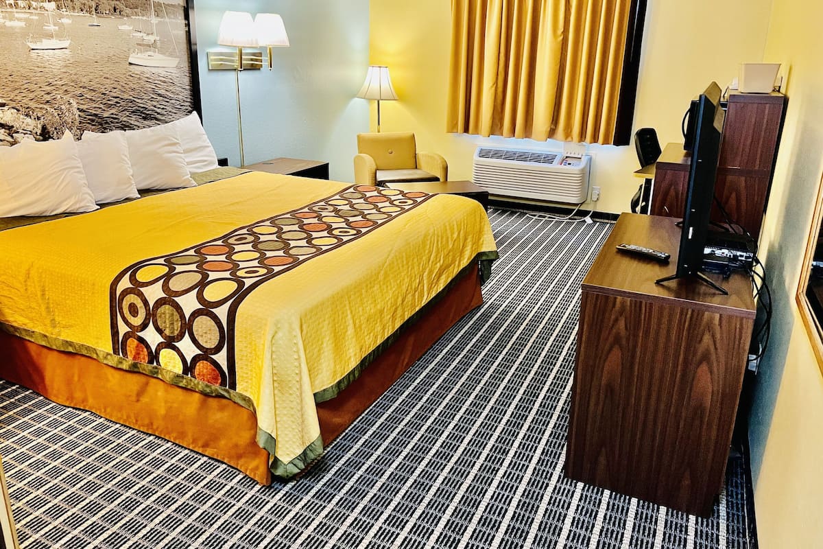Habitación de hotel con cama, escritorio, silla, televisor y aire acondicionado.