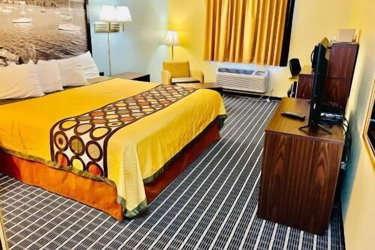 Habitación de hotel con cama, escritorio, silla, televisor y ventana con cortinas.