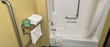 A bathroom with a bathtub, a shower, and a toilet. There are grab bars installed for safety.