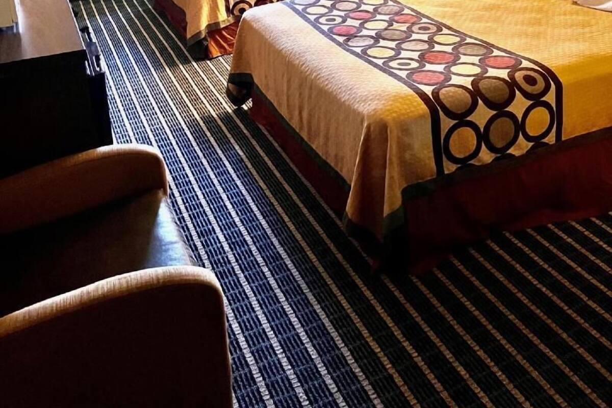 A hotel room with two beds, a desk, a chair, a window with curtains, and a painting on the wall.