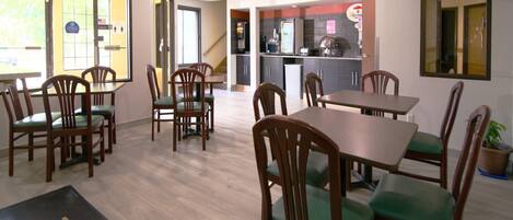 A restaurant with wooden tables and chairs, a kitchen area, and a view of the outside.
