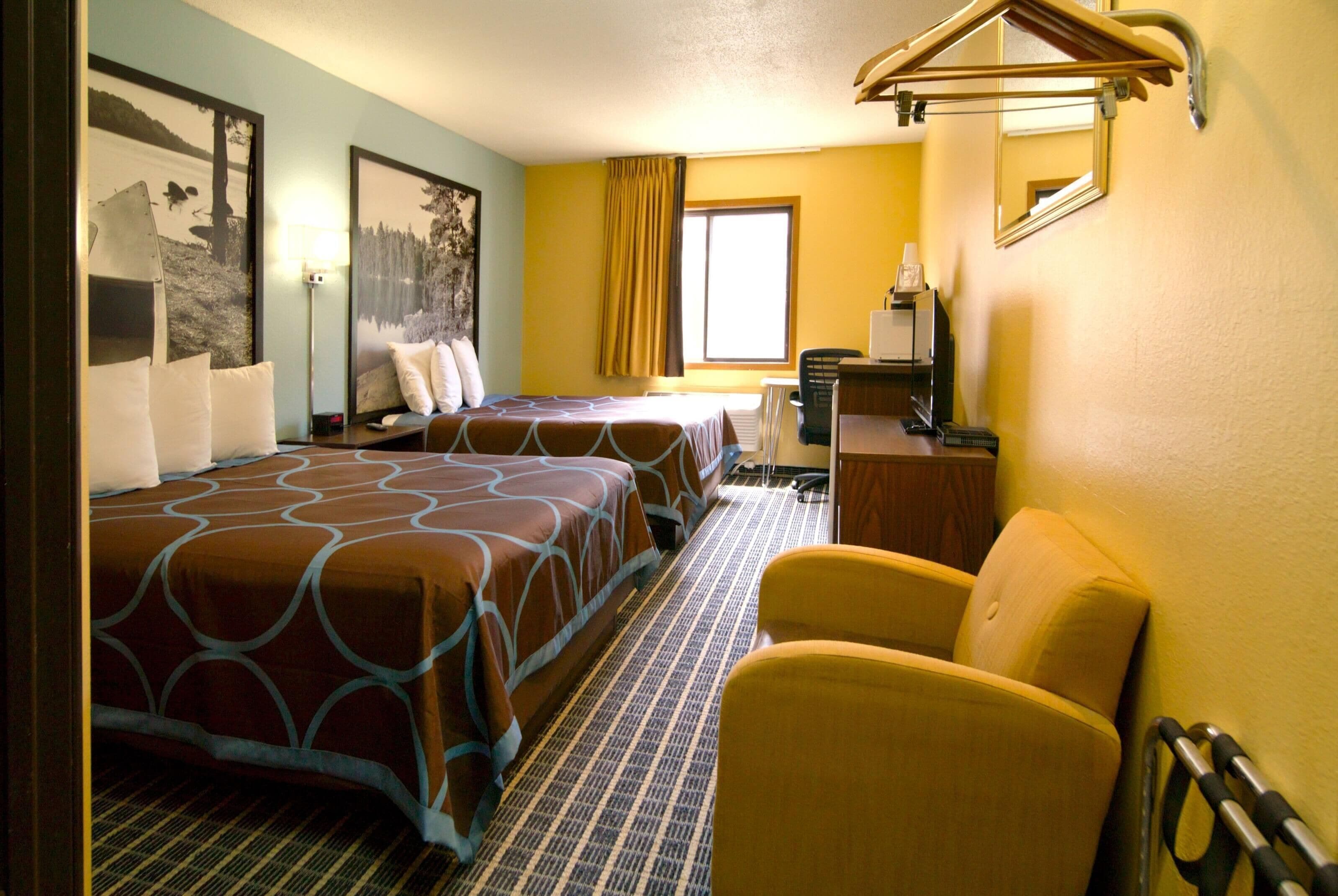A hotel room with two beds, a desk, a chair, and a window with curtains.