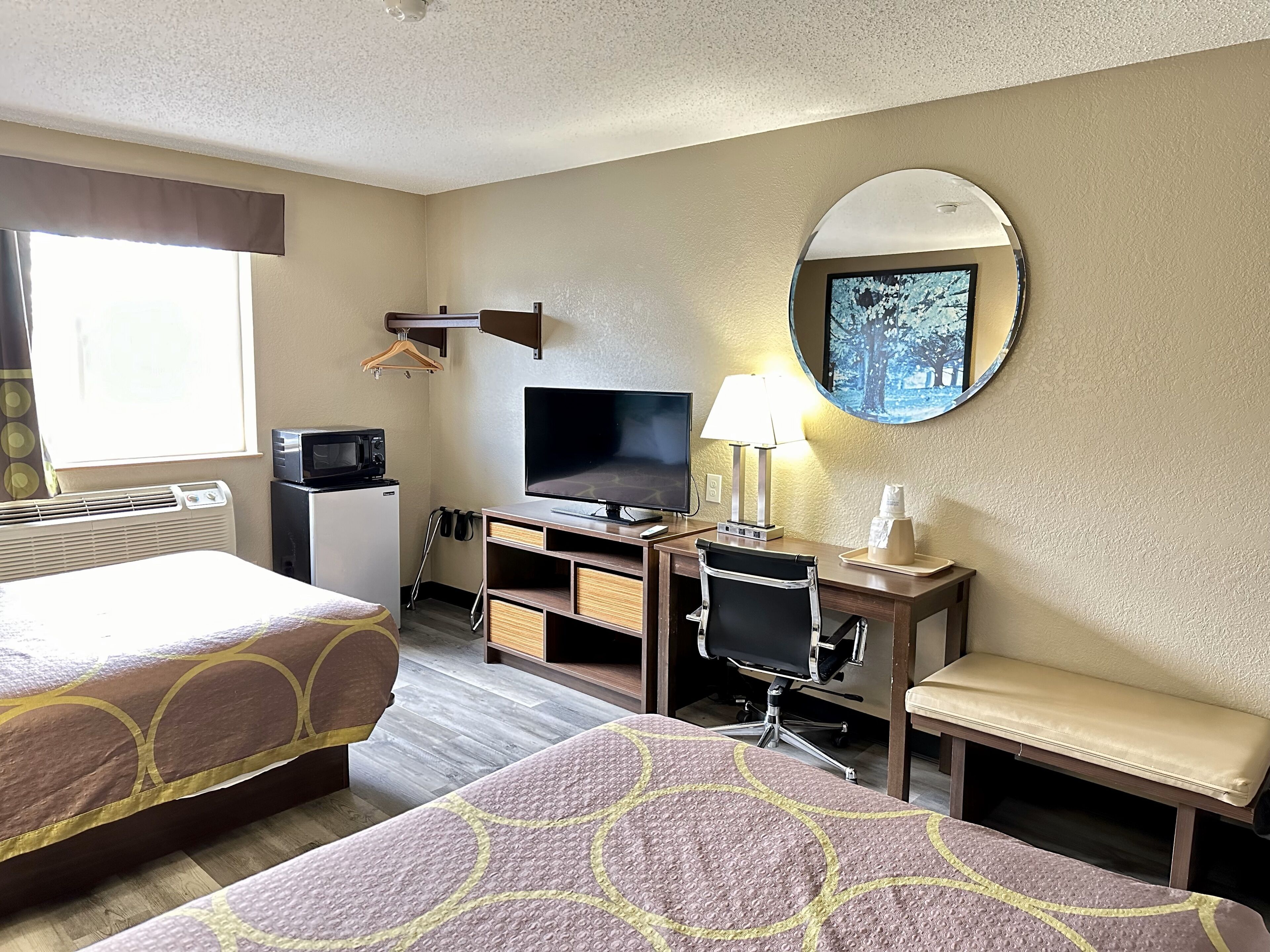 A hotel room with two beds, a desk with a computer, a TV, a lamp, and a mirror.