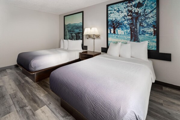 A hotel room with two beds, a nightstand with a lamp, and two wall-mounted paintings.