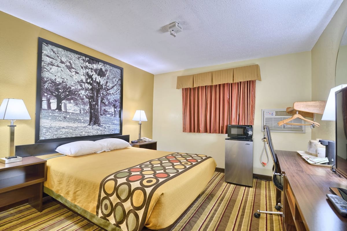 Une chambre d’hôtel comprenant un lit, deux tables de chevet, un bureau, une chaise, une télévision, un four à micro-ondes et une grande fenêtre avec des rideaux.
