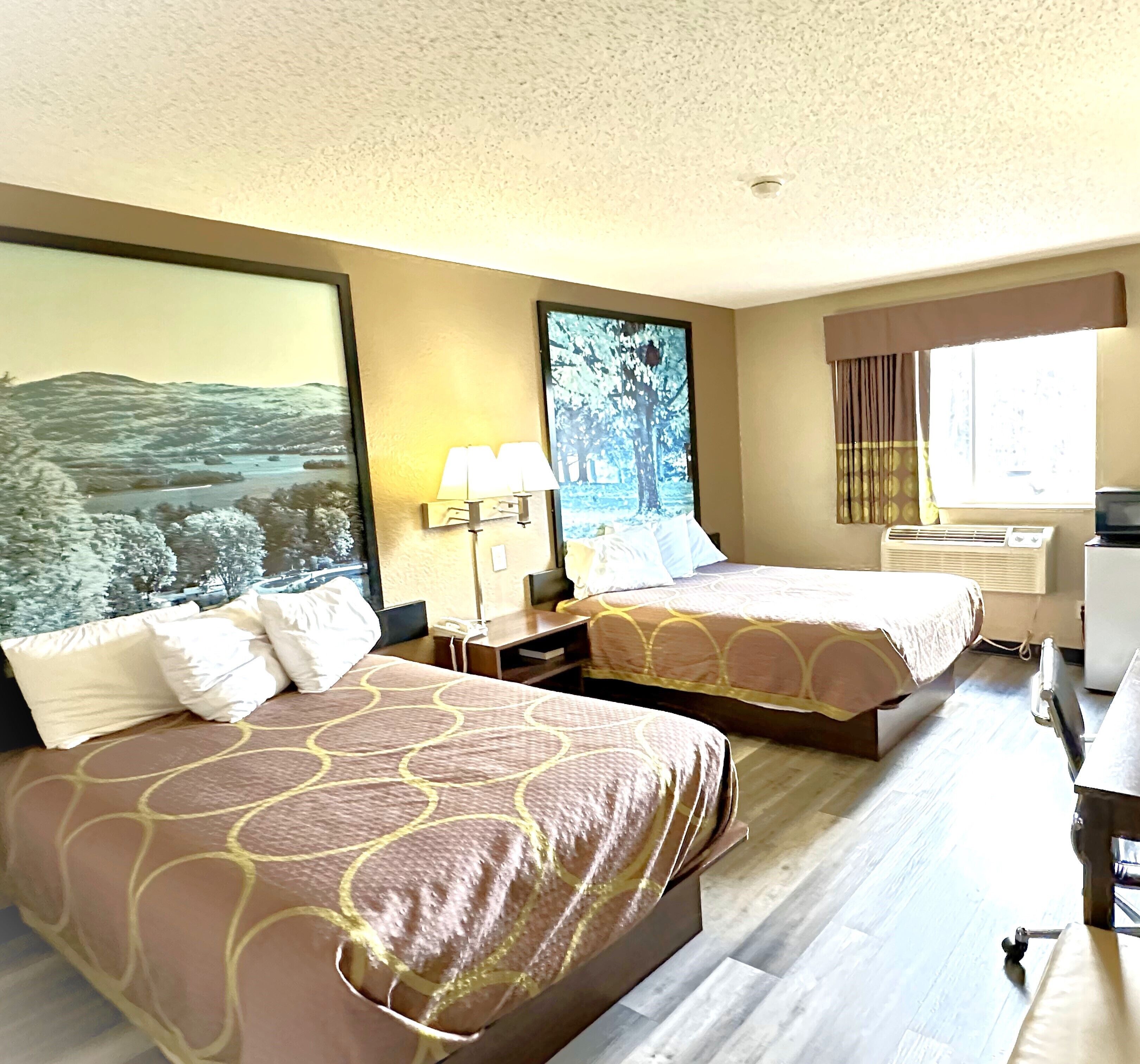 Une chambre d’hôtel avec deux lits, une grande fenêtre avec des rideaux, un bureau et un climatiseur fixé au mur.