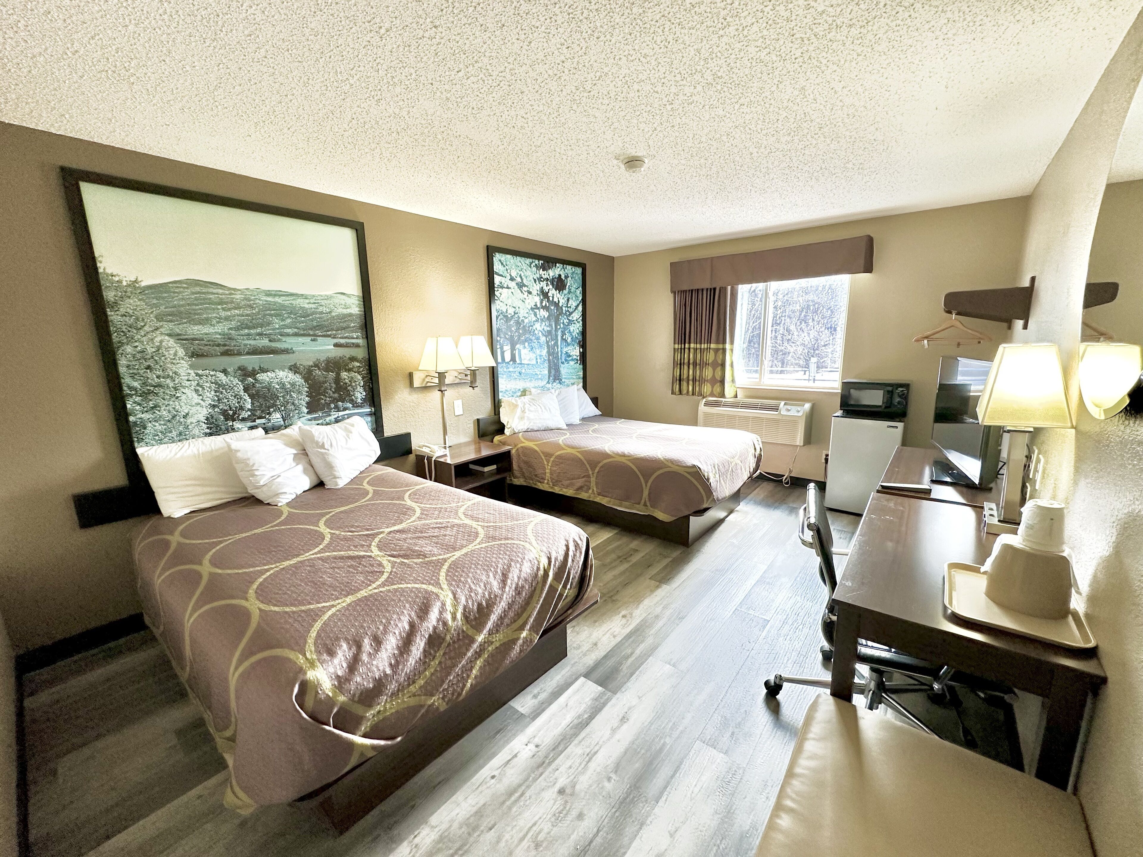 A hotel room with two beds, a desk, a chair, a TV, and a window with curtains.