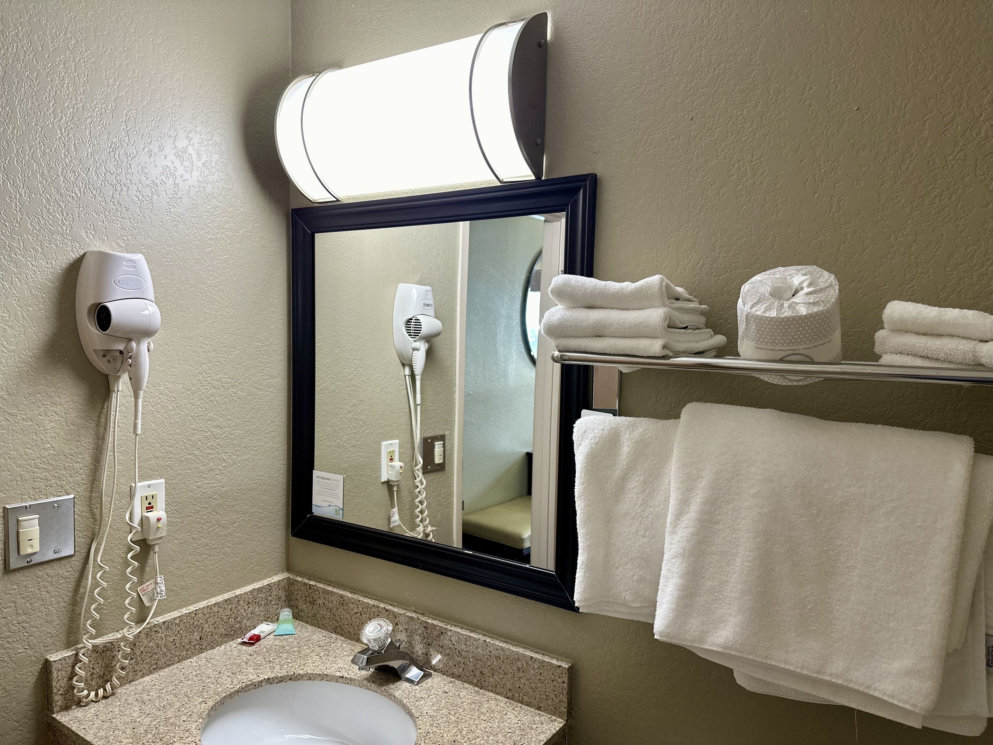 A bathroom with a sink, a mirror, a hairdryer, and a towel rack with towels.