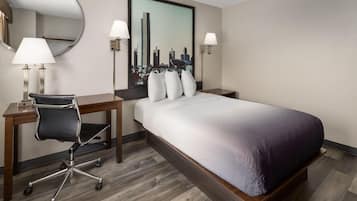 Habitación de hotel con cama, escritorio, silla, lámparas y un cuadro de paisaje urbano.