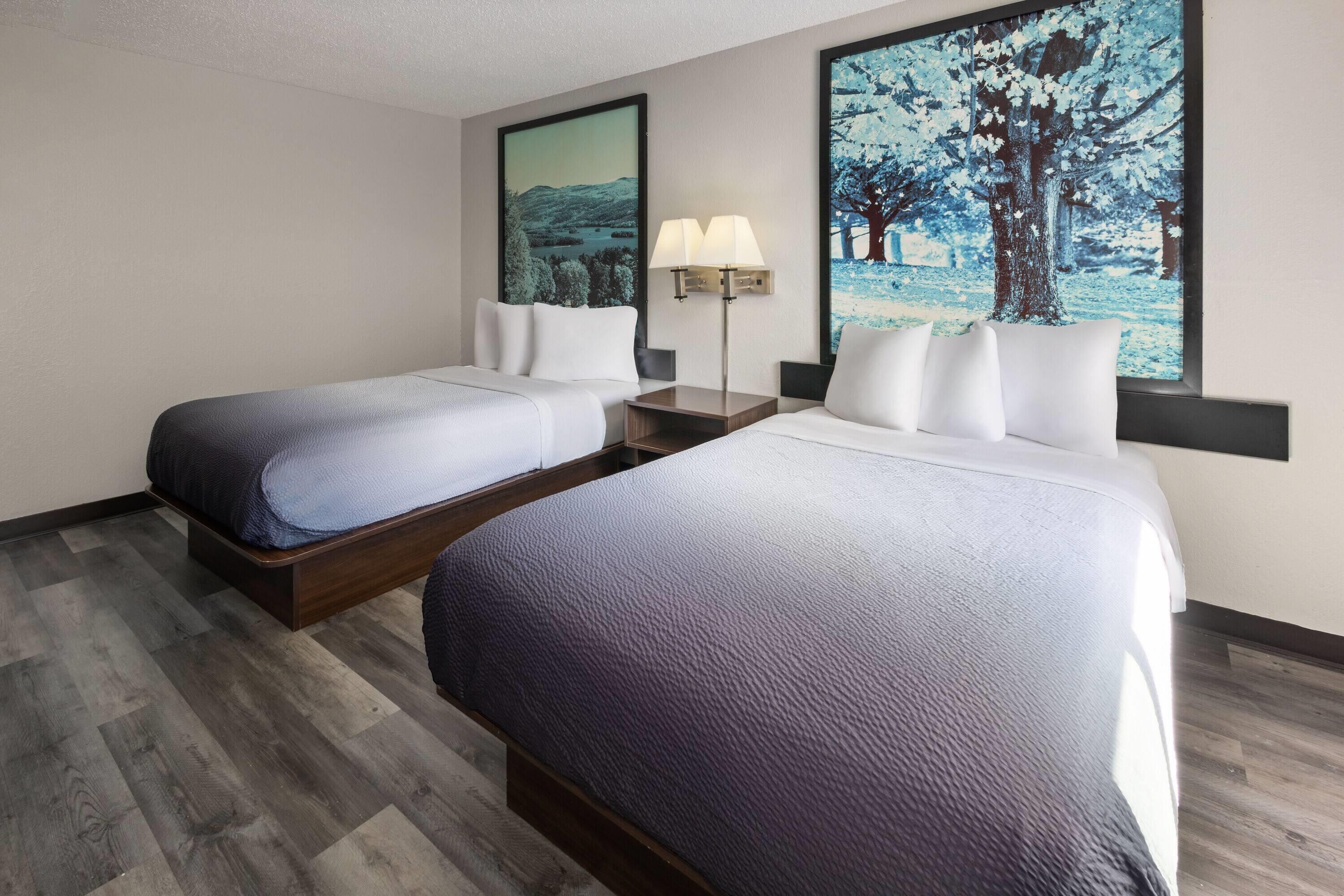 A hotel room with two beds, a nightstand with a lamp, and two framed pictures on the wall.