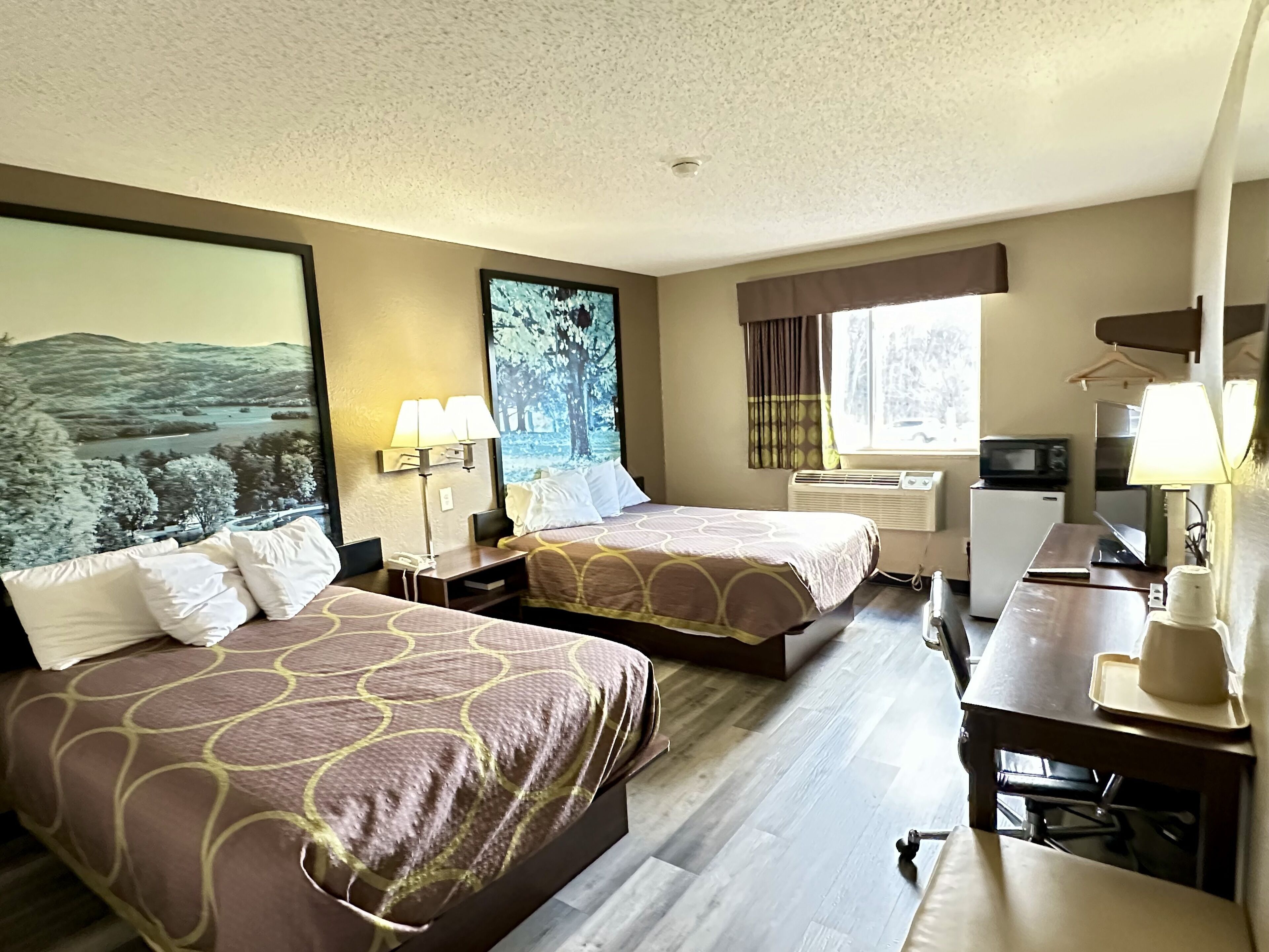 Habitación de hotel con dos camas, un escritorio, una silla, un microondas y un ventanal grande.