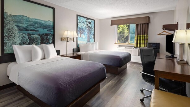 Une chambre d’hôtel avec deux lits, un bureau, une chaise, une télévision et une grande fenêtre avec des rideaux.