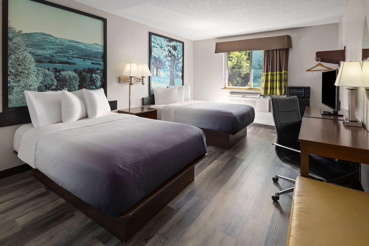 Une chambre d’hôtel avec deux lits, un bureau, une chaise, une télévision et une grande fenêtre avec des rideaux.