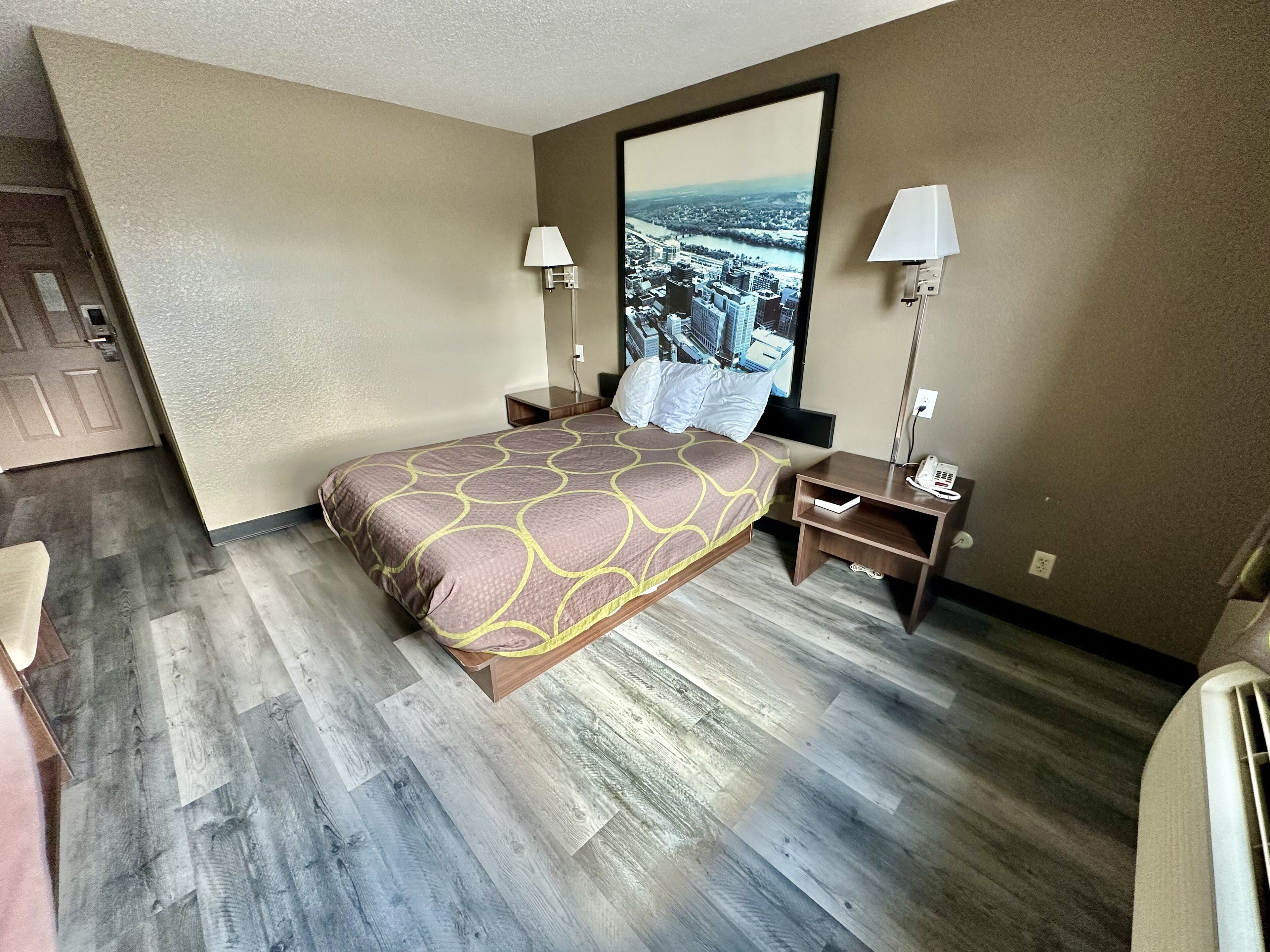 A hotel room with a bed, nightstands, lamps, and a large window with a cityscape view.
