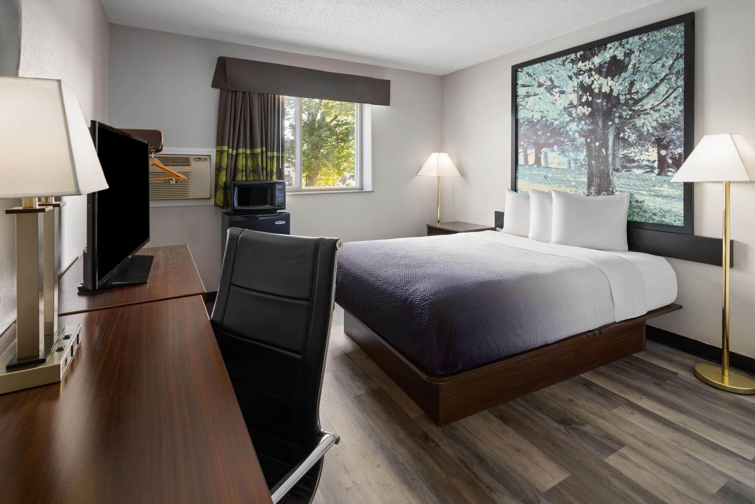 A hotel room with a bed, desk, TV, and a large window.