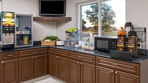 Une cuisine moderne avec des meubles de couleur marron, un four à micro-ondes encastré, une machine à café et une grande fenêtre donnant sur l’extérieur.
