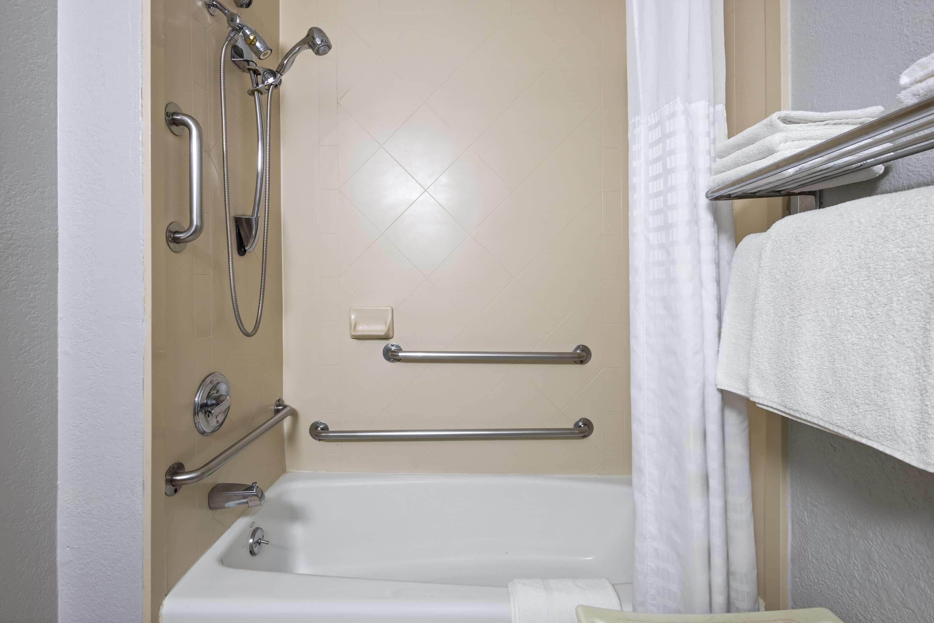A bathroom with a bathtub, grab bars, a showerhead, and a towel rack.