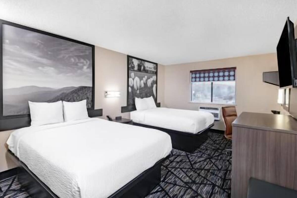 A hotel room with two beds, a desk, a chair, a television, and artwork on the walls.