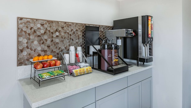 A breakfast bar with a honeycomb-patterned backsplash, a coffee machine, and a beverage dispenser. - Super 8 by Wyndham Charlottesville (Charlottesville)