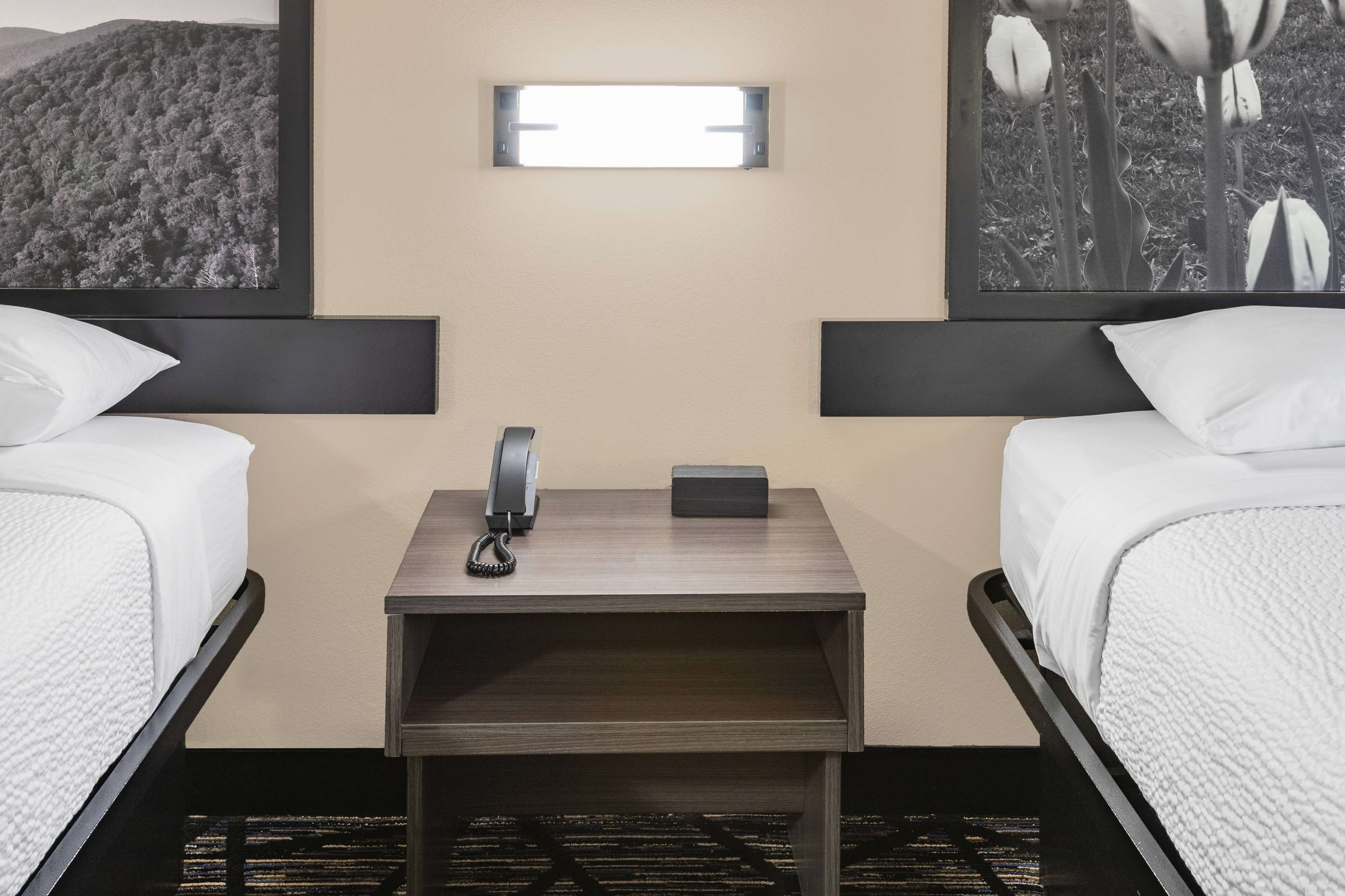 A hotel room with two single beds, a bedside table with a telephone and a small box, and a wall-mounted light fixture.