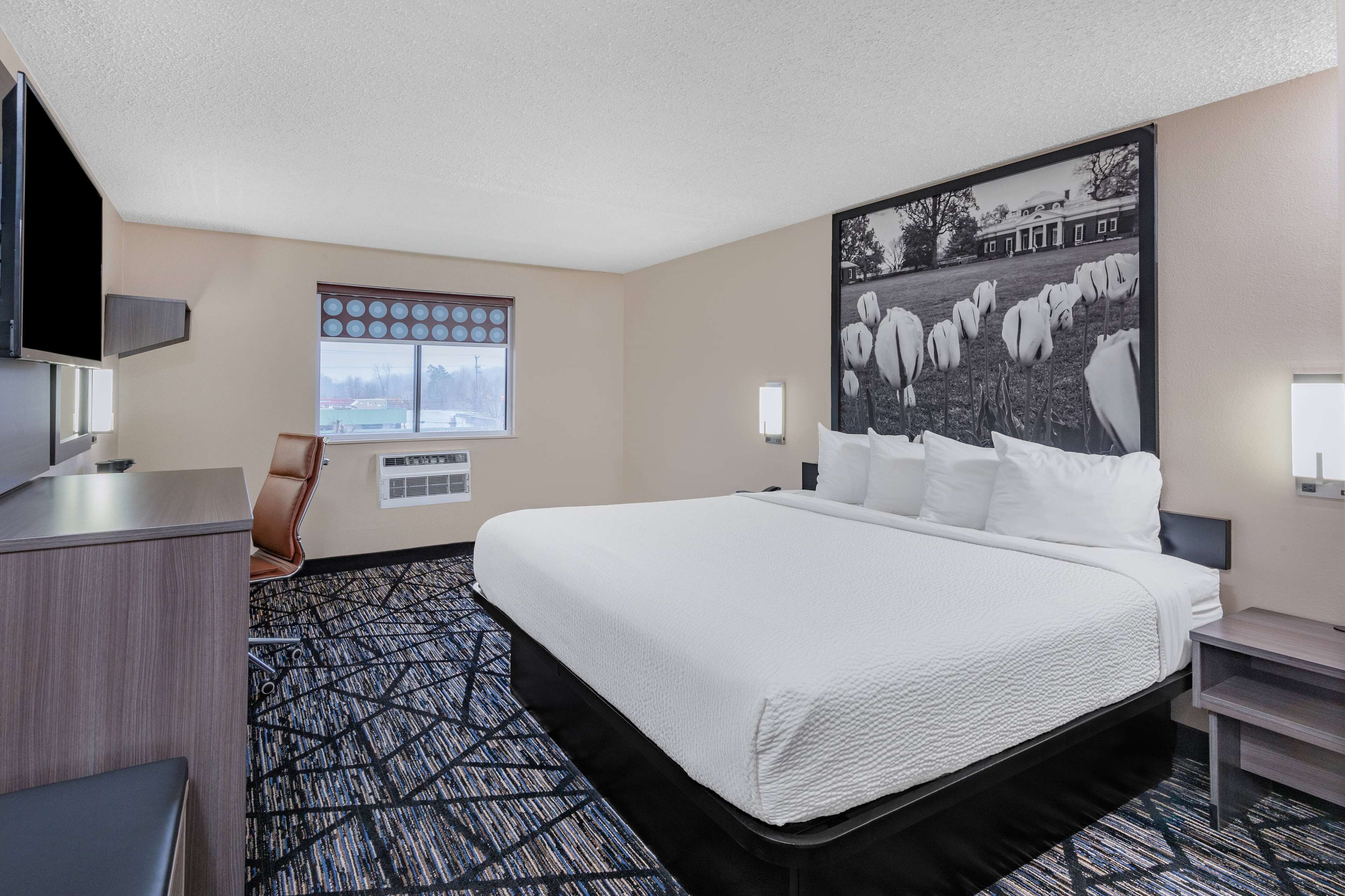 A hotel room with a large bed, a desk, a chair, a window with a view, and a wall-mounted TV.
