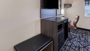 A hotel room with a flat-screen TV mounted on the wall, a desk with a chair, and a window with a view. - Super 8 by Wyndham Charlottesville (Charlottesville)