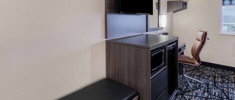 A hotel room with a flat-screen TV mounted on the wall, a desk with a chair, and a window with a view.