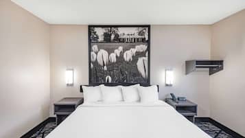 A hotel room with a large bed, two bedside tables, a mounted air conditioner, and a framed picture on the wall.