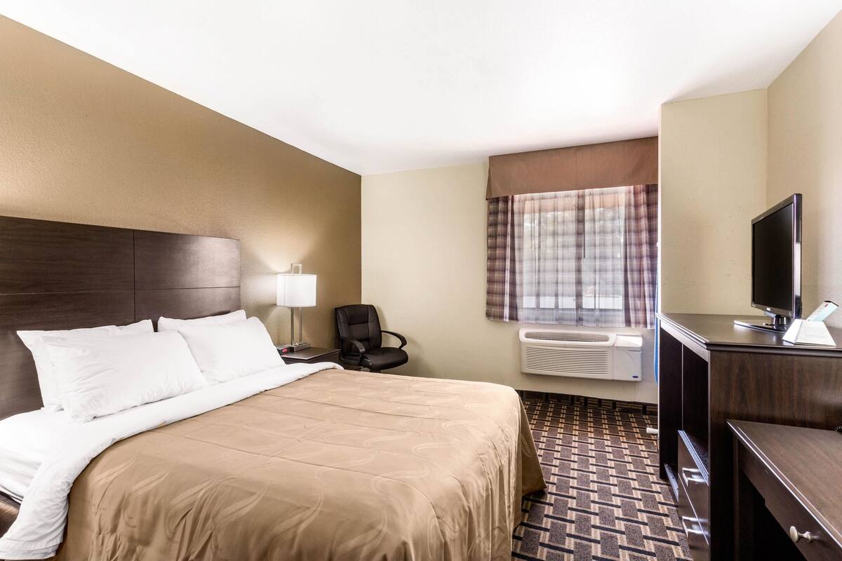 Une chambre d’hôtel avec un grand lit, un bureau avec un ordinateur, une chaise, une télévision et un appareil de climatisation.